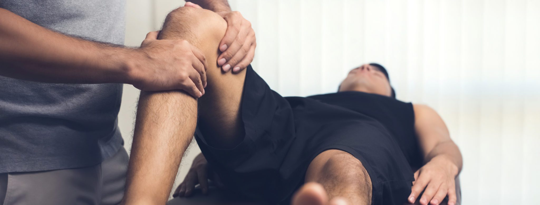 Bilden föreställer en naprapat, kiropraktor eller terapeut som undersöker en knäled på en patient.